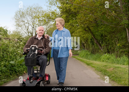 Heureusement mariée mature couple en promenade dans la campagne alors que l'un conduit un scooter de mobilité motorisée Banque D'Images