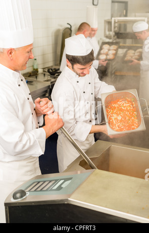 Chef cuisinier professionnel avec l'équipe de préparer des aliments en cuisine industrielle Banque D'Images