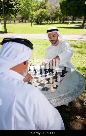 Fils adultes arabes jouant aux échecs avec le père dans le parc, en souriant. Banque D'Images