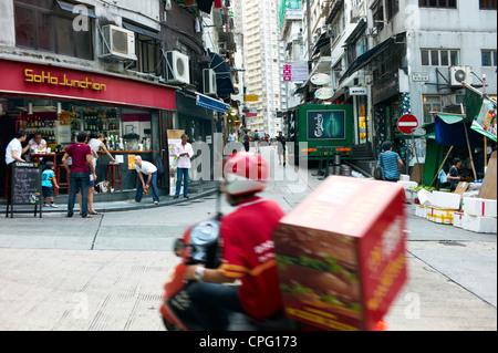 Une personne livraison courses par une intersection achalandée à Soho, Central Hong Kong. Banque D'Images