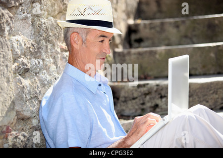 Un homme âgé est assis sur les marches avec portable Banque D'Images