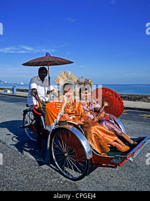 La Malaisie. Penang. Deux femmes en vêtements traditionnels équitation de pousse-pousse. Banque D'Images