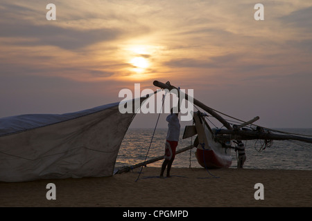 Pêcheur Prendre en bas la voile de son Oruvas, une pirogue à balancier, sur la plage de Negombo, Sri Lanka, Asie Banque D'Images