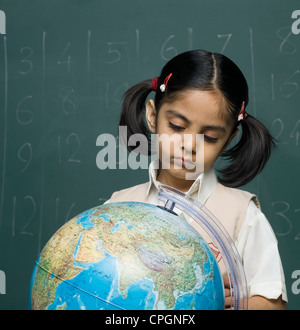 Girl (6-7) in classroom looking at globe Banque D'Images