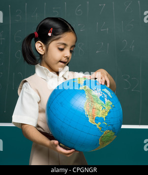 Girl (6-7) in classroom looking at globe Banque D'Images