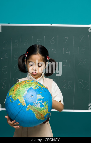 Girl (6-7) in classroom looking at globe Banque D'Images