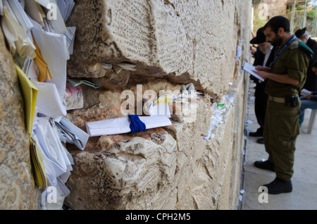 Notes de papier dans une fissure avec soldat israélien en train de prier. Mur ouest. Vieille ville de Jérusalem. Israël. Banque D'Images