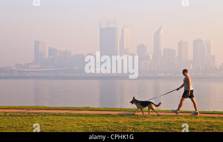 Homme marchant un chien en bas à côté du chemin River avec la silhouette d'un horizon brumeux dans l'arrière-plan. Banque D'Images