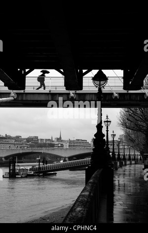 Vue des pluies de l'imprimeur de la marche prend sous le pont ferroviaire et Hungerford Golden Jubilee Passerelle, South Bank, Londres, UK Banque D'Images