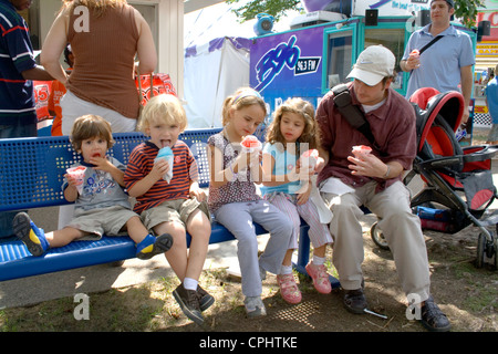 Quatre jeunes enfants mangeant cônes de neige sur banc avec père. Minnesota State Fair St Paul Minnesota MN USA Banque D'Images