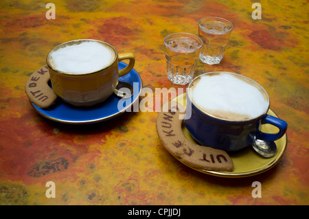 Deux tasses de café mousseux sur une table avec des biscuits et deux verres d'eau Banque D'Images