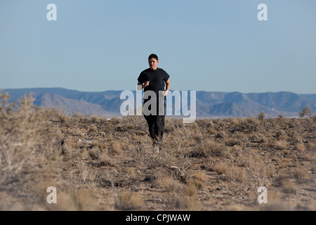 Hispanique athlétique jeune homme qui traverse le désert à Albuquerque, Nouveau Mexique, porter tout noir. Banque D'Images