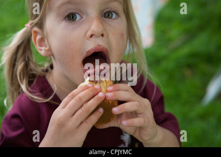 Quatre ans, fille de lécher le glaçage d'un cupcake. Banque D'Images