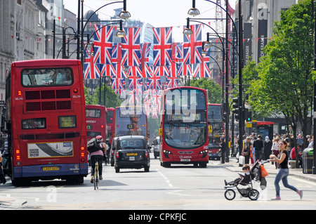 Bus taxi et vélo à Oxford Street Londres West End Angleterre UK Union Jacks pour 2012 Jeux Olympiques et mère traversant la route enfant dans poussette Banque D'Images