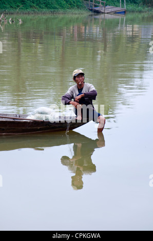 Pêcheur en barque d'une traction en résille. Assis et de l'équilibre sur le bord des bateaux et le tabagisme Banque D'Images