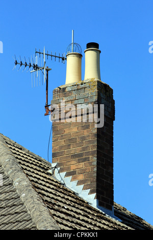 Cheminée sur toit de tuiles avec antenne, fond de ciel bleu. Banque D'Images