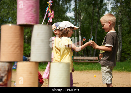 Les enfants lancent avec petite balle sur la pyramide de boîtes de conserve Banque D'Images