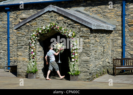 Jeune homme portant des fleurs dans le porche de l'église St Martin, Bowness, Parc National de Lake District, Cumbria, Angleterre, Royaume-Uni Banque D'Images