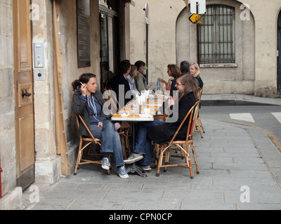 Les femmes assises et fumer des cigarettes à des tables sur le trottoir dans un café à Paris, France, 9 mai 2012, © Katharine Andriotis Banque D'Images