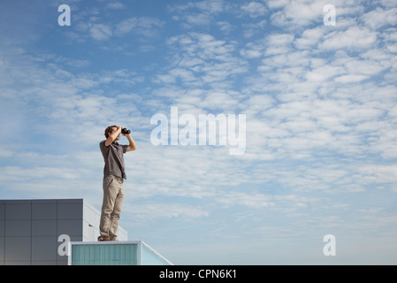 Homme debout sur le toit surdimensionné, binoculars Banque D'Images