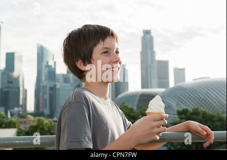 Boy holding ice cream cone, toits de la ville en arrière-plan Banque D'Images