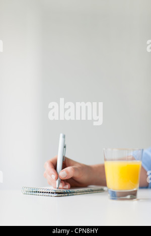 Woman writing on notepad à côté de verre de jus d'orange Banque D'Images