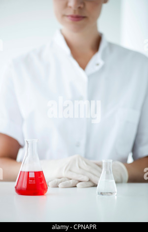 Fioles coniques en laboratoire, femme portant des gants en latex en arrière-plan Banque D'Images