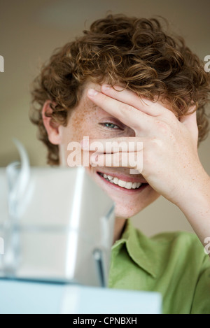 Boy peeking through fingers à wrapped gifts Banque D'Images