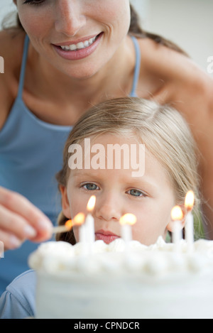 Girl comme sa mère s'allume les bougies sur le gâteau d'anniversaire Banque D'Images