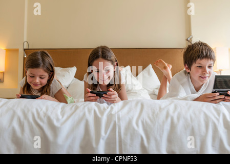 Siblings playing handheld video games on bed Banque D'Images