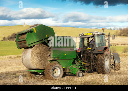 La mise en balles de paille avec McHale et balles rondes tracteur Massey Ferguson. Banque D'Images