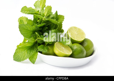 Bol avec limes et un bouquet de menthe sur fond blanc Banque D'Images