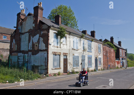 Un homme sur un scooter de mobilité depuis une ligne de disques durs délabré et abandonné de maisons abandonnées dans la région de Sheffield, South Yorkshire, Angleterre Banque D'Images