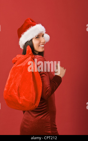 Belle fille de Noël avec des cadeaux sac sur un fond rouge. Banque D'Images