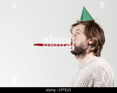 Mid adult man avec soufflante parti contre fond blanc Banque D'Images