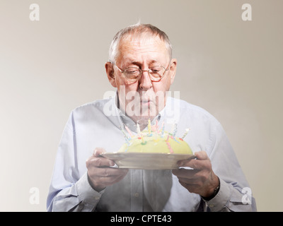 Senior man blowing out candles on cake anniversaire m against white background Banque D'Images