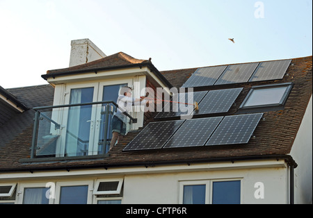 Nettoyer la poussière de sa femme panneaux solaires avec un balai sur le toit de la maison, promenade Sussex UK Banque D'Images