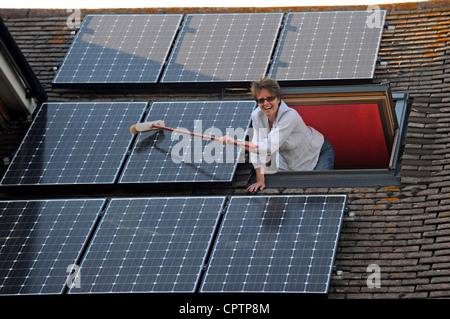 Nettoyer la poussière de sa femme panneaux solaires avec un balai sur le toit de la maison, promenade Sussex UK Banque D'Images