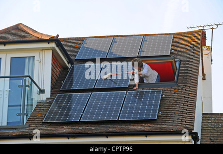 Nettoyer la poussière de sa femme panneaux solaires avec un balai sur le toit de la maison, promenade Sussex UK Banque D'Images