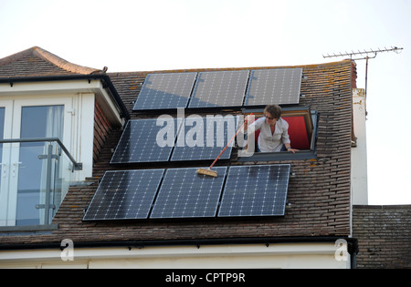 Nettoyer la poussière de sa femme panneaux solaires avec un balai sur le toit de la maison, promenade Sussex UK Banque D'Images