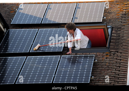 Nettoyer la poussière de sa femme panneaux solaires avec un balai sur le toit de la maison, promenade Sussex UK Banque D'Images