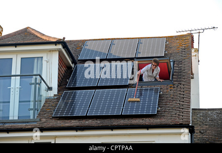 Nettoyer la poussière de sa femme panneaux solaires avec un balai sur le toit de la maison, promenade Sussex UK Banque D'Images