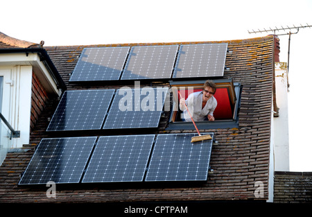 Nettoyer la poussière de sa femme panneaux solaires avec un balai sur le toit de la maison, promenade Sussex UK Banque D'Images