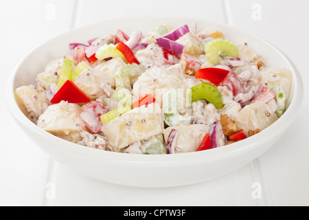 Salade de pommes de terre et de poivron rouge, oignon rouge, le céleri et les noix dans un miel moutarde, mayonnaise, sur un tableau blanc. Banque D'Images