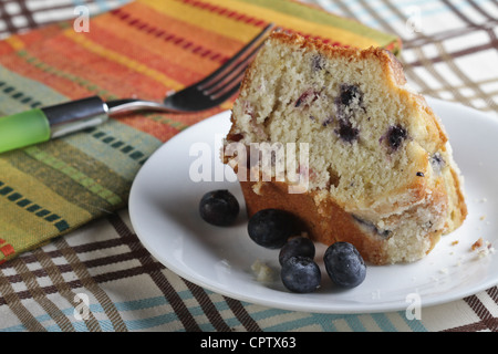 Une tranche de gâteau aux bleuets sur un endroit libre sur une nappe à rayures colorées avec une serviette et un chariot avec une poignée verte. Banque D'Images