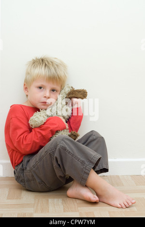 Enfant solitaire assis sur le plancher à l'aide d'un jouet. Banque D'Images