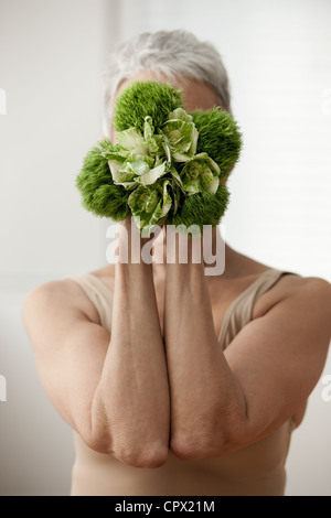 Senior woman holding plant in front of face Banque D'Images