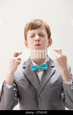 Boy wearing costume gris avec les doigts croisés, studio shot Banque D'Images