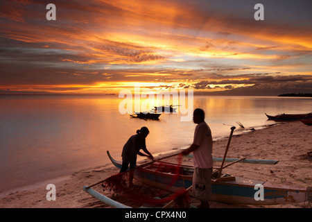 Pêcheur & woman tending moustiquaires au crépuscule sur la plage de San Juan, les Visayas, Siquijor, Philippines Banque D'Images