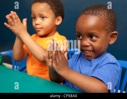 Deux enfants assis à un bureau tapant dans leurs mains Banque D'Images